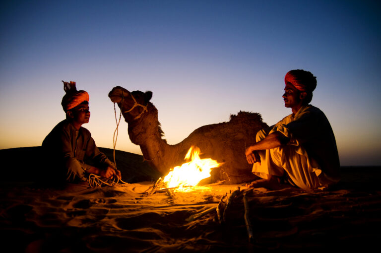 indian men resting by the bonfire with their camel